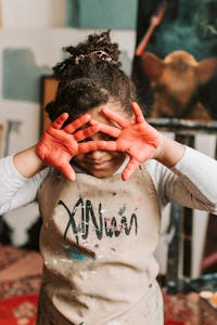 Young child with red-painted hands enjoying art in a cozy studio setting.